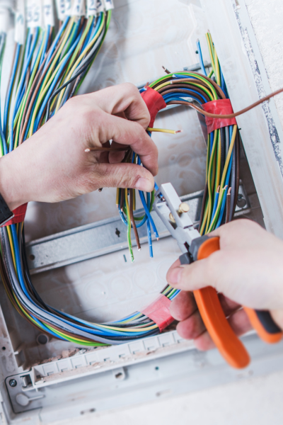 Electrician uses wire strippers to prepare cables inside an electrical panel for installation.