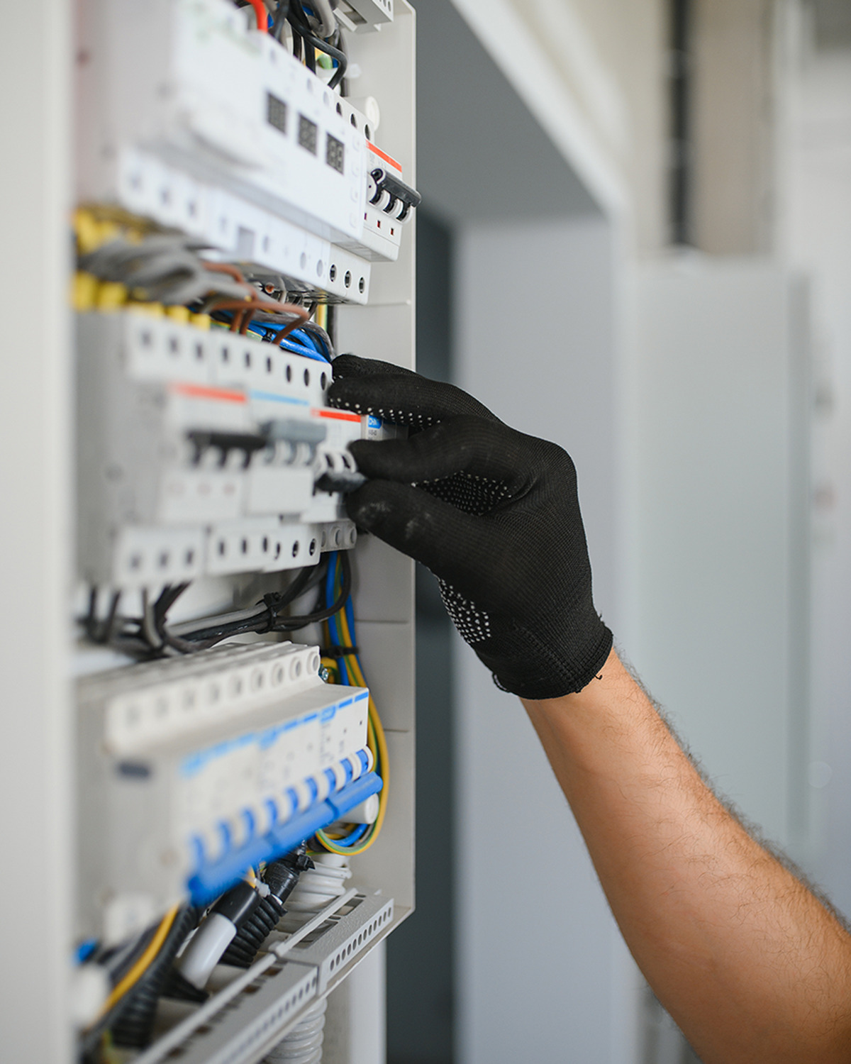 Male electrician working on a switchboard, adjusting components while wearing protective gloves.