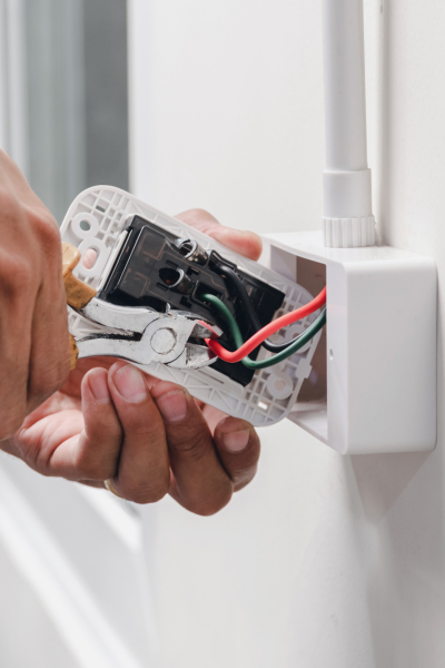 Electrician using pliers to connect wires while replacing an electrical outlet, showing detailed wiring.