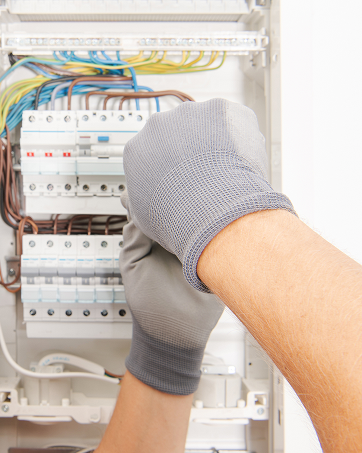 Electrician wearing a red cap and gray gloves working on an apartment fusebox installation.