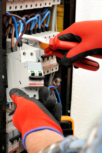 Electrician performing emergency repair on an electrical panel, using insulated tools and wearing protective gloves.