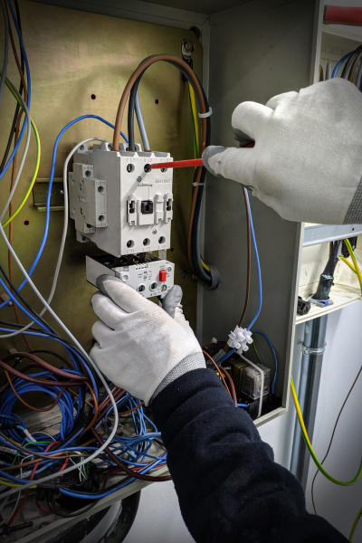 Electrician replacing components in an electrical panel, using a screwdriver and wearing protective gloves.