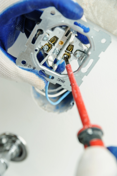 Electrician using a screwdriver to secure wires in an electrical outlet, wearing blue and white gloves.