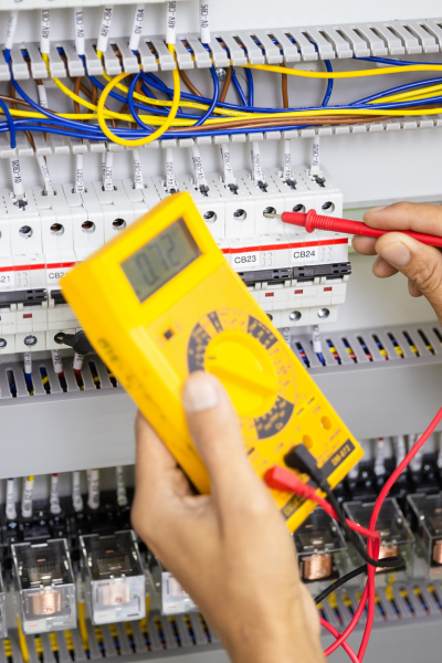 Electrician using a multimeter to perform a safety inspection and load capacity on an electrical panel, checking voltage levels.