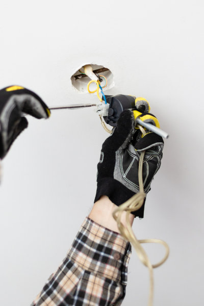 Electrician fixing faulty wiring in a wall using a screwdriver.