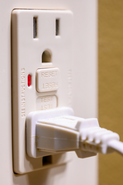 Close-up of a GFCI electrical outlet with a plug inserted, showing the reset and test buttons.