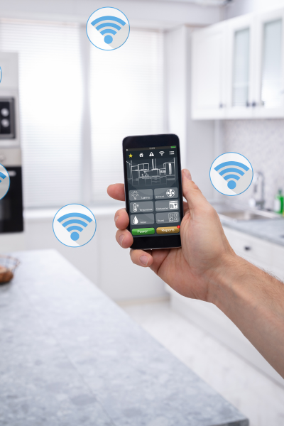 Hand holding a smartphone with a smart home control app, connected to various Wi-Fi-enabled devices in a modern kitchen.