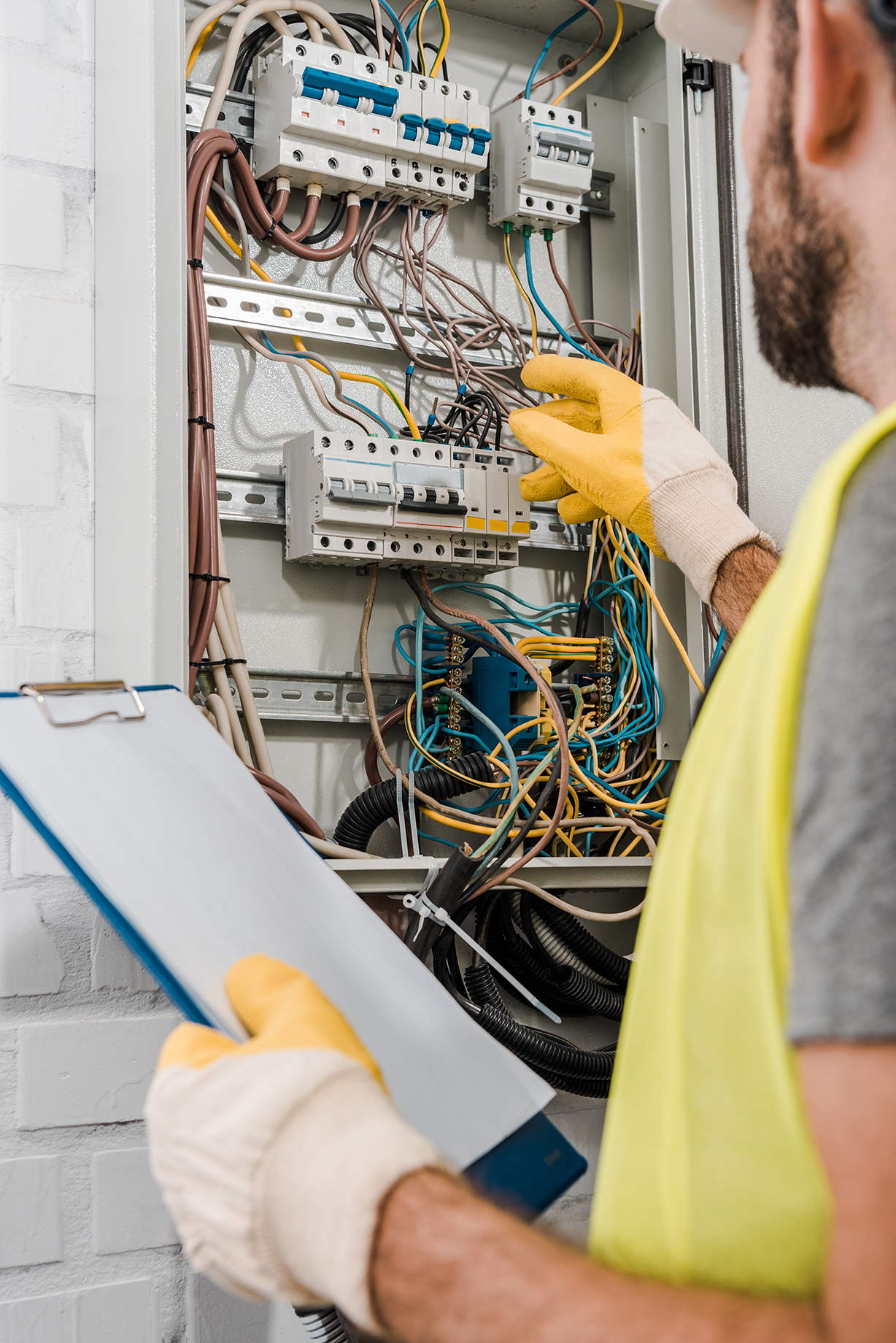 Electrician in safety gear inspecting and working on a complex electrical panel, ensuring proper wiring and circuit connections.