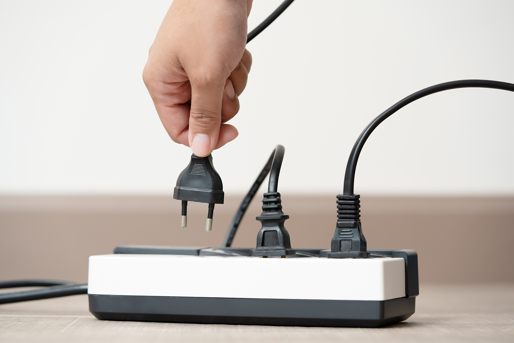 Hand plugging or unplugging an electric cord into a power strip, demonstrating safe electrical maintenance practices.